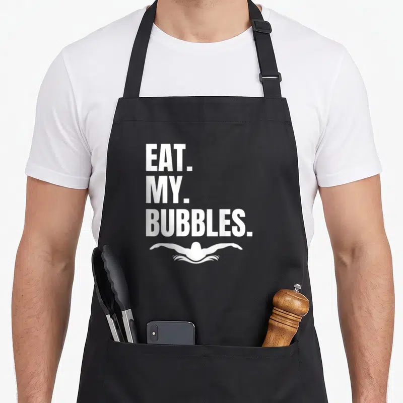 Eat swimmer apron - EAT MY BUBBLES text above white swimmer silhouette in minimalist style — shown on a black cotton canvas apron against a white background