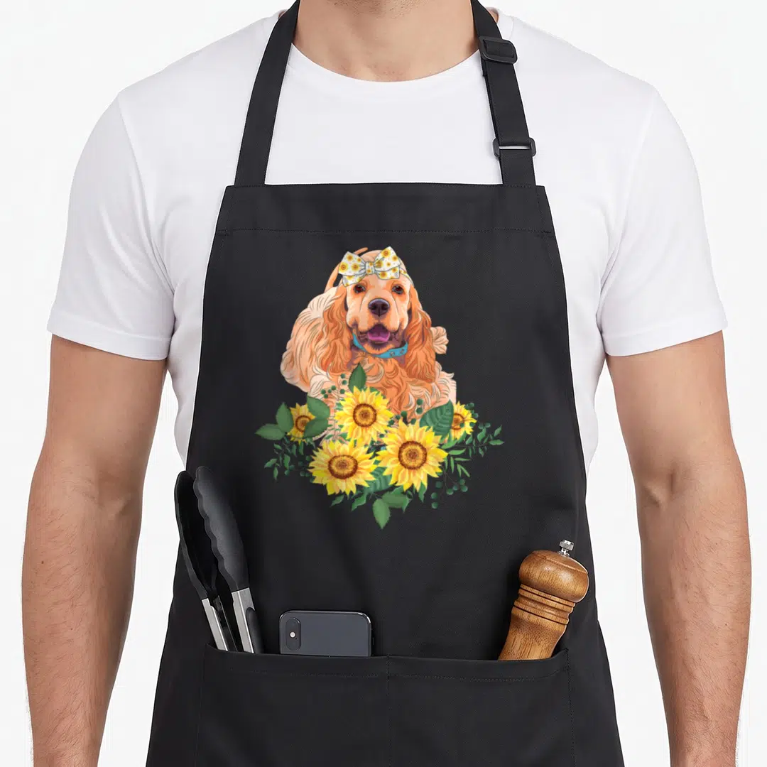 Sunflower cocker spaniel apron - Cartoon ginger dog with blue collar and floral bow surrounded by yellow sunflowers — shown on a black cotton canvas apron against a white background