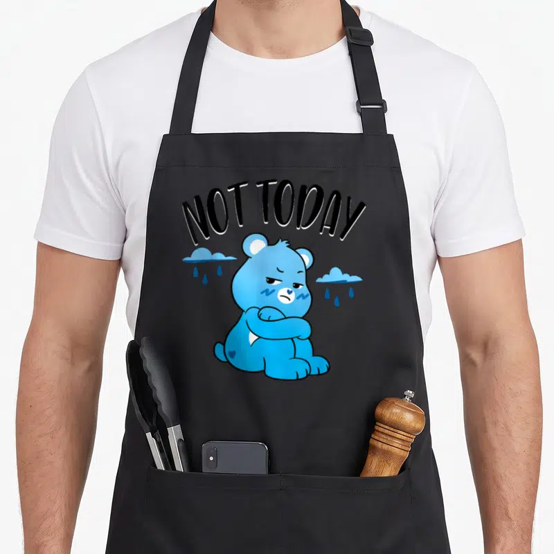 Unlock magic apron - Grumpy blue bear with crossed arms under NOT TODAY text and rain clouds — shown on a black cotton canvas apron against a white background