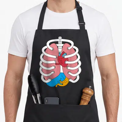 Hugging organ apron - Cartoon white ribcage arms hugging pink lungs, red heart, and blue yellow organs — shown on a black cotton canvas apron against a white background