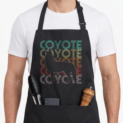 Funny coyote apron - Retro stacked COYOTE text in teal yellow orange red pink with grey coyote outline — shown on a black cotton canvas apron against a white background