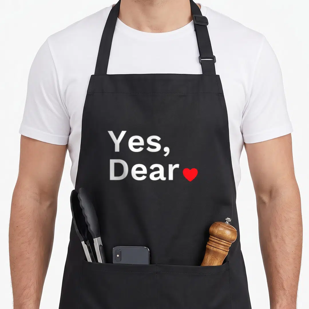 Funny dear valentine apron - White Yes, Dear text stacked with a small red heart on the right side — shown on a black cotton canvas apron against a white background