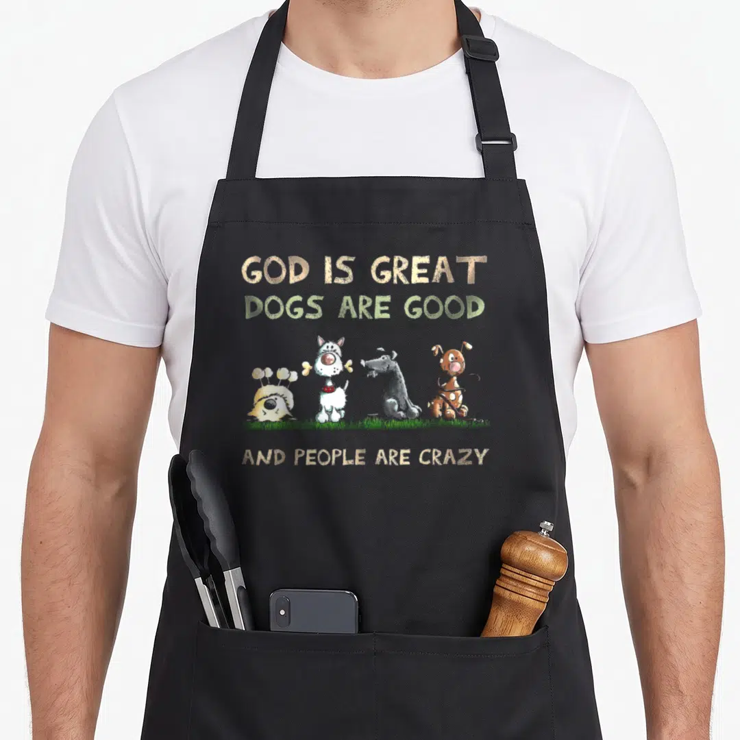 God dog apron - Four cartoon dogs standing on grass under text about gods and crazy people — shown on a black cotton canvas apron against a white background