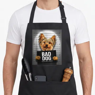 Mugshot yorkie apron - Dog holding black sign with Bad Dog Police Dep text in front of height chart — shown on a black cotton canvas apron against a white background