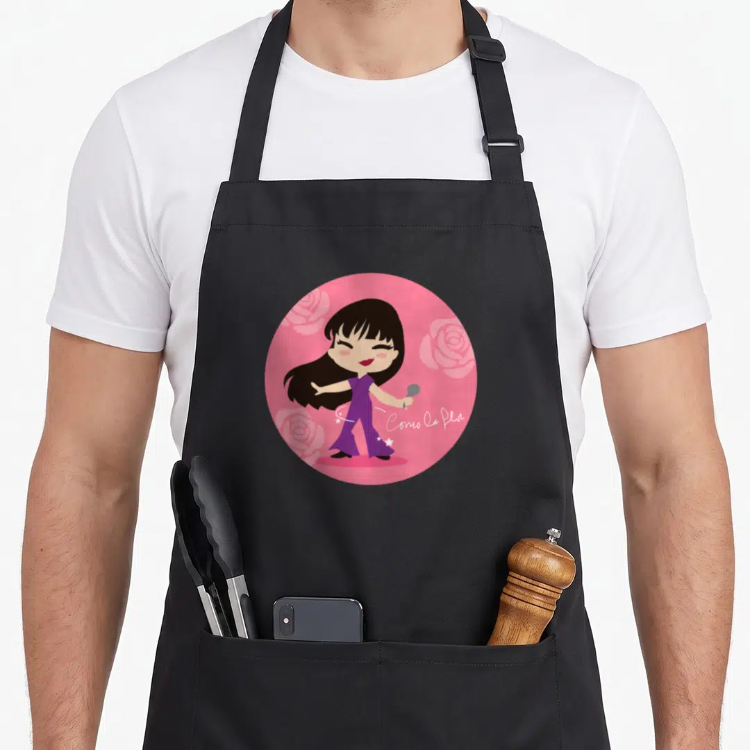 Como cumbia apron - Cartoon woman in purple holding mic in pink circle with roses and Como la Flor text — shown on a black cotton canvas apron against a white background