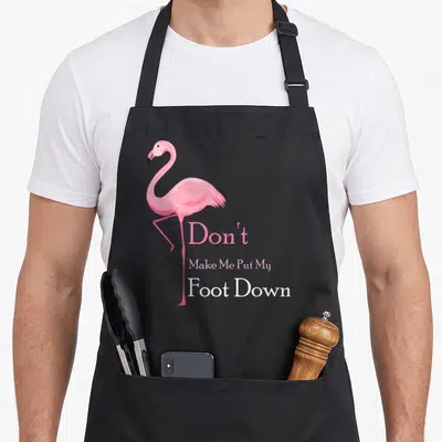 Vintage bird pink flamingo apron - Standing pink flamingo next to stacked text reading Don't Make Me Put My Foot Down — shown on a black cotton canvas apron against a white background
