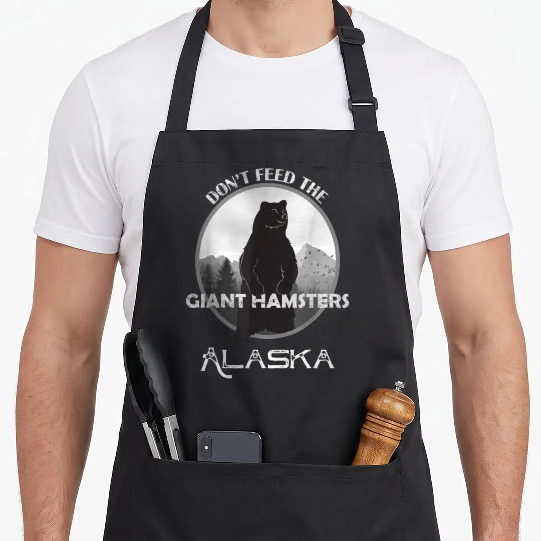 Alaskan grizzly bear apron - Black bear silhouette in grey circle with Don't Feed The Giant Hamsters Alaska text — shown on a black cotton canvas apron against a white background