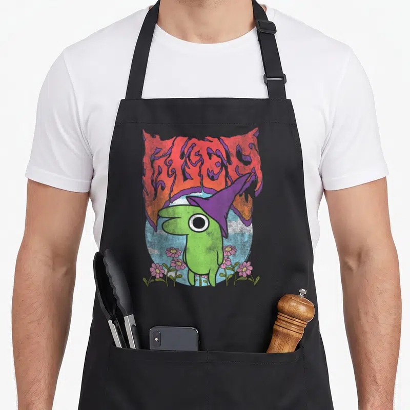 Smiling heavy apron - Green creature purple hat BLEED text pink flowers light blue circle cartoon art — shown on a black cotton canvas apron against a white background