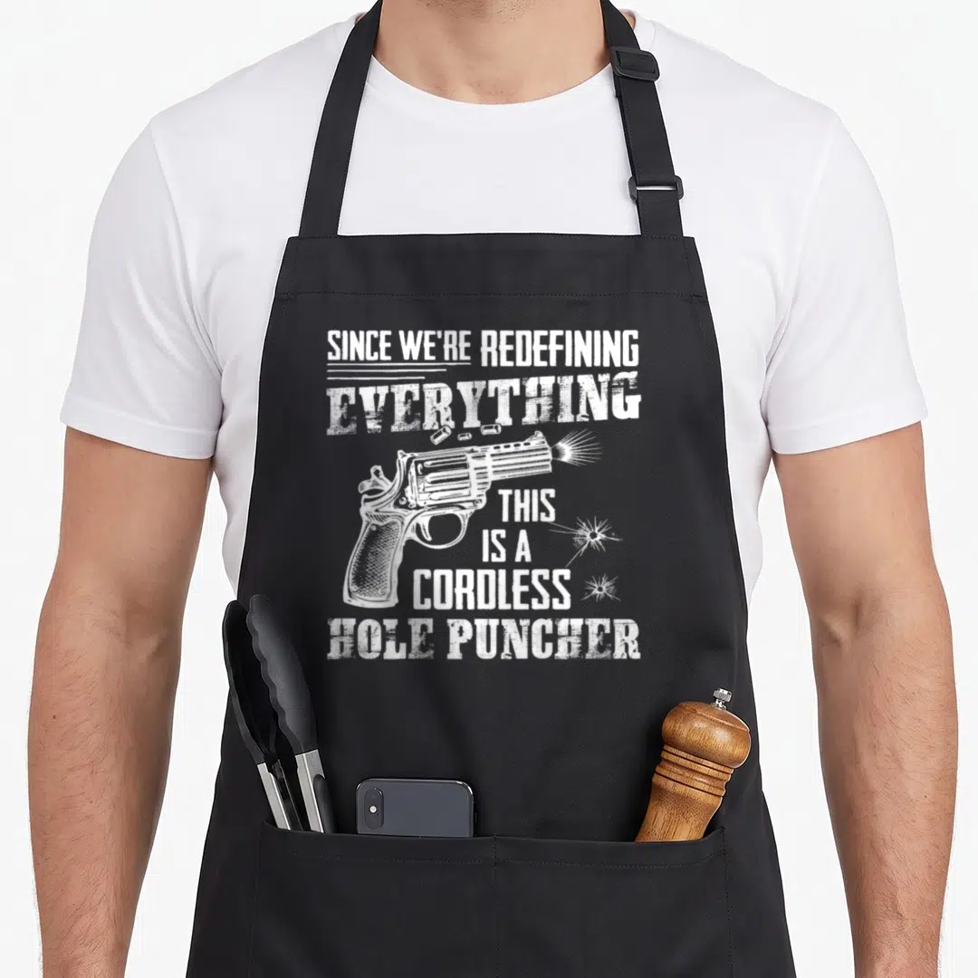 Meme 2nd apron - White distressed revolver illustration with text SINCE WE'RE REDEFINING, EVERYTHING, THIS IS — shown on a black cotton canvas apron against a white background