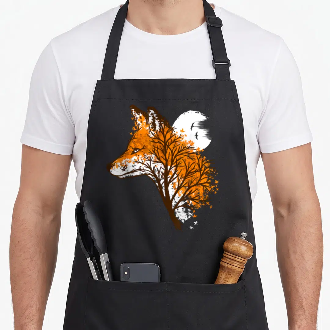 Beautiful fox print apron - Orange fox profile formed by brown tree branches with white moon and two birds — shown on a black cotton canvas apron against a white background