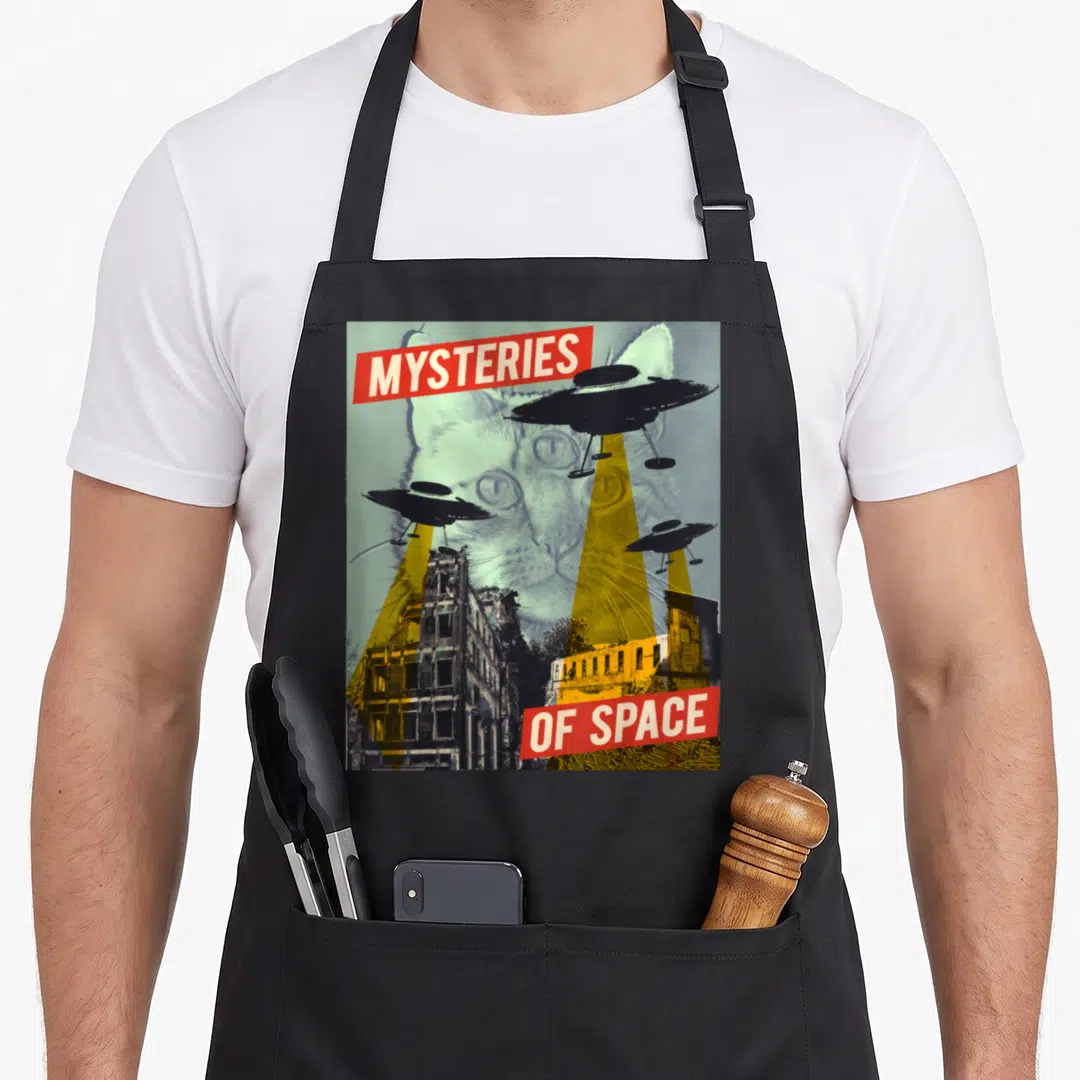 Flying cat apron - Retro poster with large cat face, three UFOs, yellow beams, and red banners reading Mysteries — shown on a black cotton canvas apron against a white background