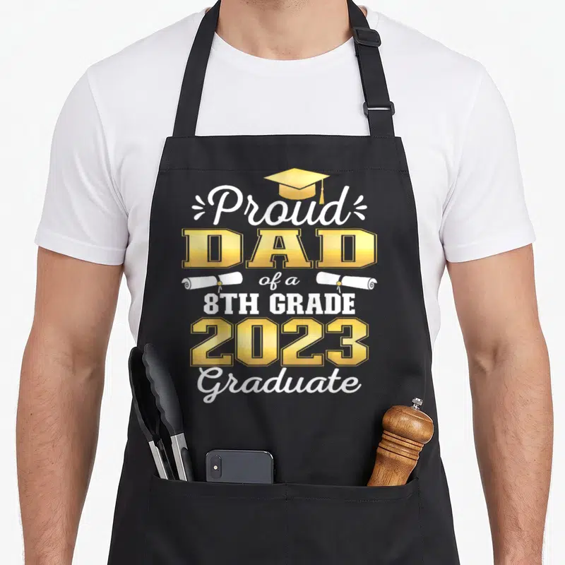 8th family aprons - Yellow graduation cap and two white diplomas flanking stacked text reading Proud Dad of a 8th Grade — shown on a black cotton canvas apron against a white background