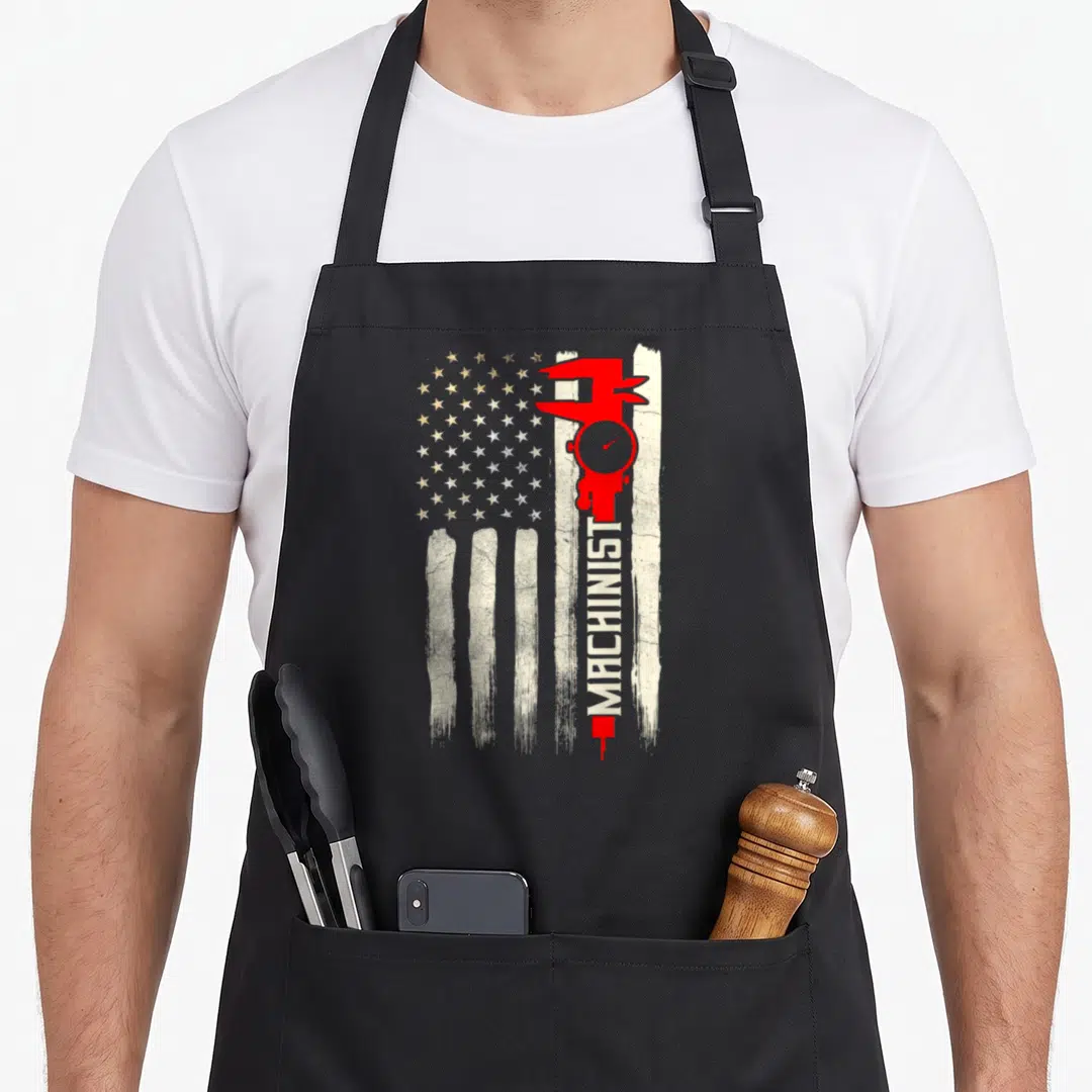 Patriotic machinist apron - Red caliper with vertical MACHINIST text over distressed white stripes and gold stars — shown on a black cotton canvas apron against a white background