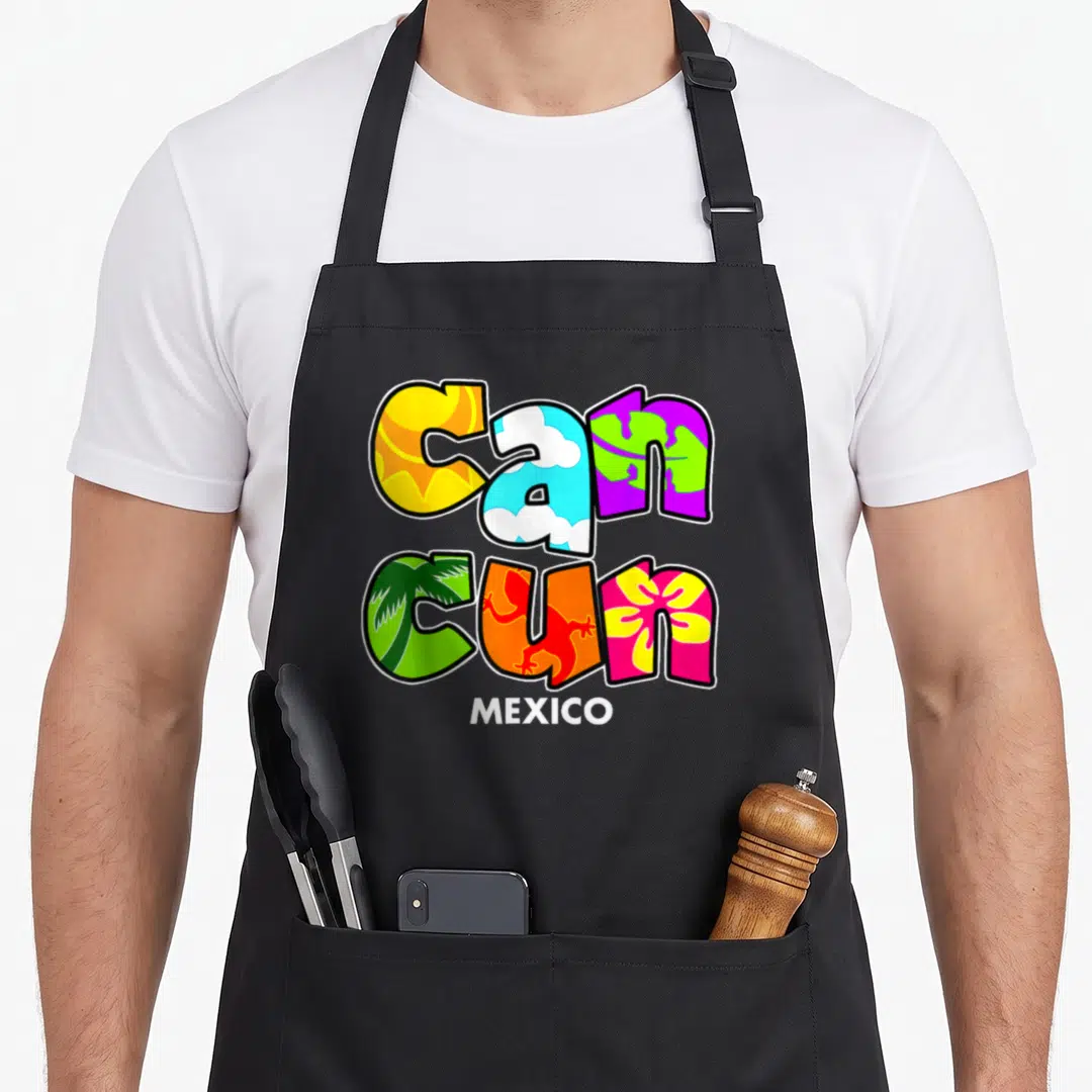 Spring mexico apron - Colorful CANCUN text filled with sun, clouds, palm, lizard, and flower illustrations above white — shown on a black cotton canvas apron against a white background