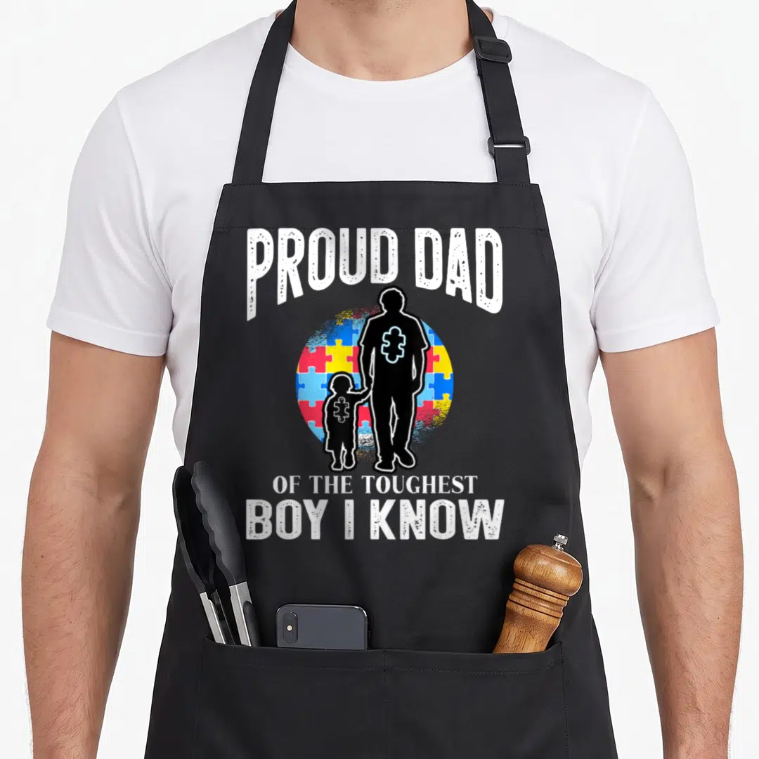 Proud autism dad apron - Black silhouette of father and son holding hands in front of a blue red yellow and blue puzzle — shown on a black cotton canvas apron against a white background