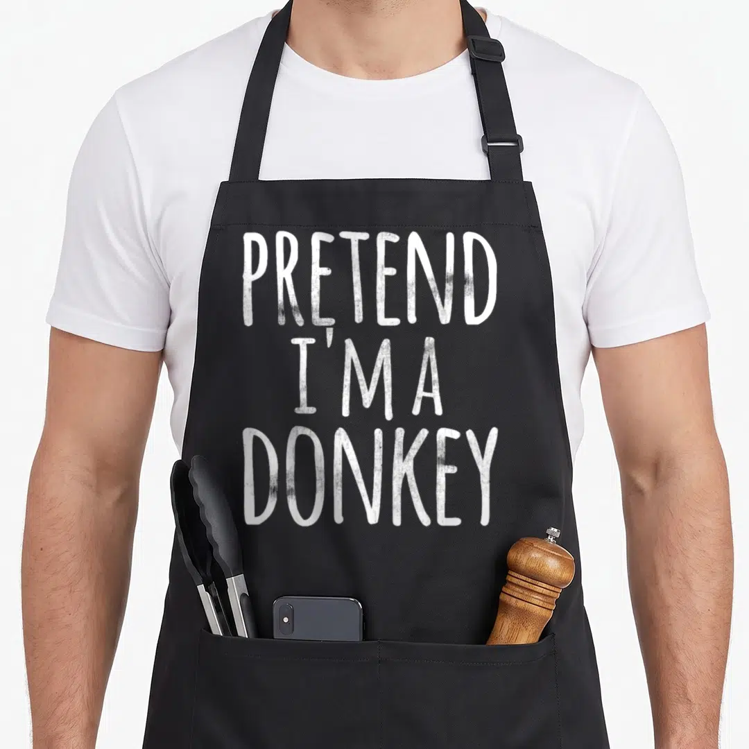 Easy halloween apron - White stacked text reading PRETEND I'M A DONKEY on grey background — shown on a black cotton canvas apron against a white background
