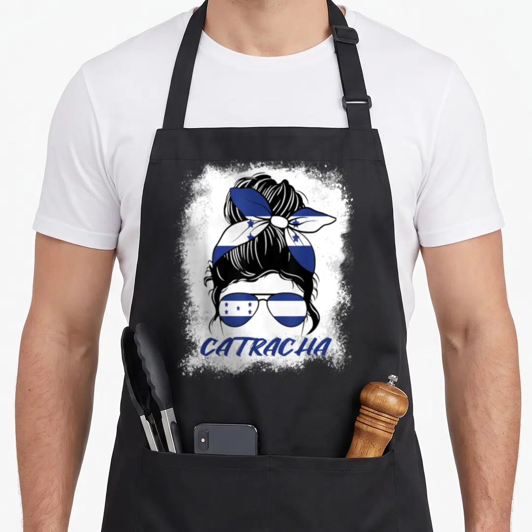 Catracha honduran apron - Stylized woman head with bun and sunglasses in blue white flag pattern with CATRACHA text — shown on a black cotton canvas apron against a white background