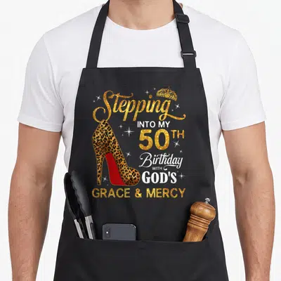 50th grace apron - Leopard high heel shoe with Stepping Into My 50th Birthday with God's Grace and Mercy text — shown on a black cotton canvas apron against a white background