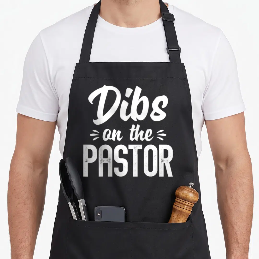 Dib wife apron - White stacked text Dibs on the PASTOR in script and block fonts with distressed finish — shown on a black cotton canvas apron against a white background