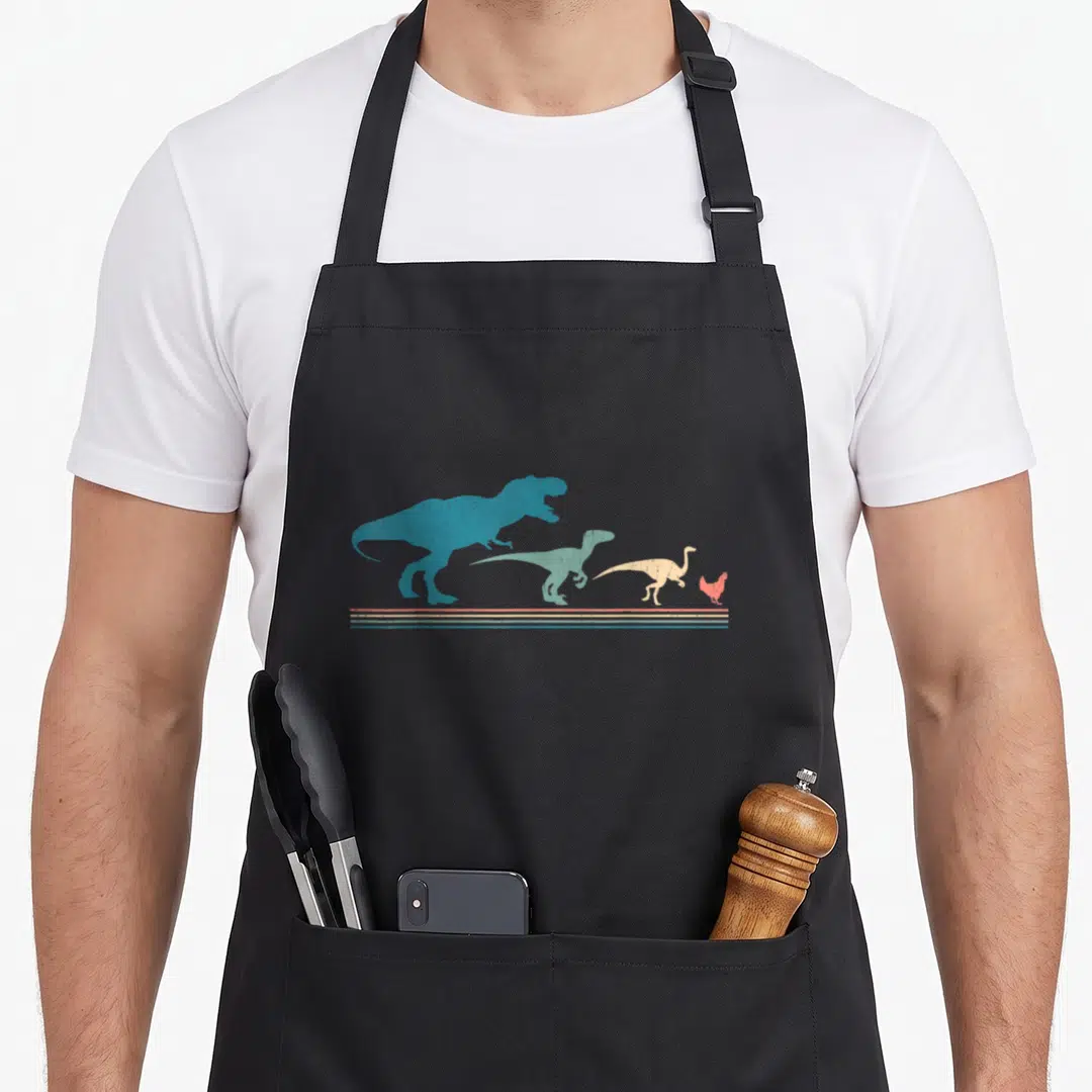 Dinosaur chicken apron - Four dinosaurs shrinking to a chicken in blue teal beige and red with horizontal stripes below — shown on a black cotton canvas apron against a white background