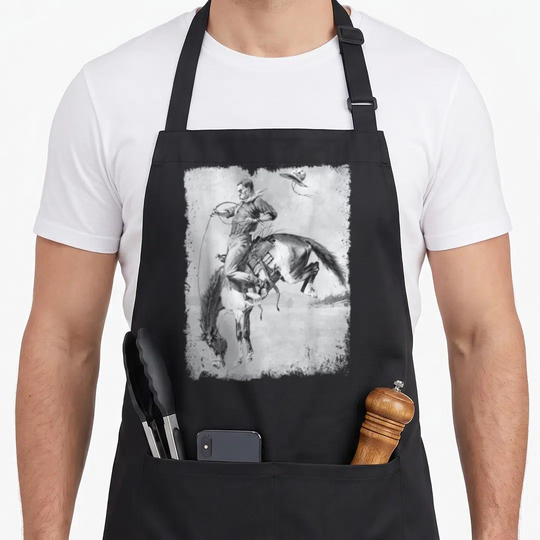 Horse cowboy apron - Realistic cowboy riding bucking horse with flying hat in distressed grey frame — shown on a black cotton canvas apron against a white background