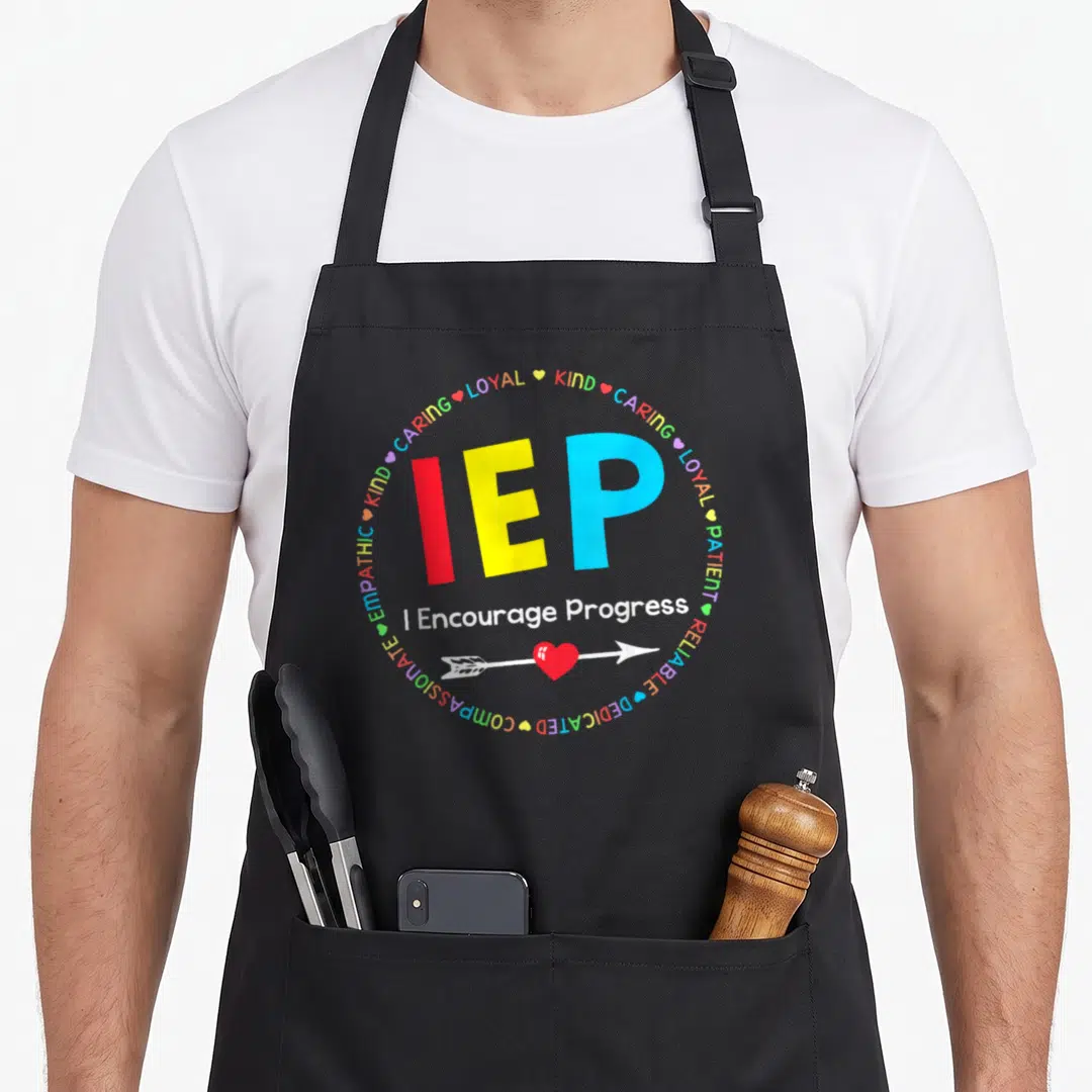 Encourage progress special teacher apron - IEP in red yellow blue with circle of kind caring loyal words and I — shown on a black cotton canvas apron against a white background