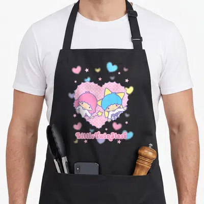 Twin valentine apron - Two cartoon characters inside pink polka-dot heart with scattered stars and text below — shown on a black cotton canvas apron against a white background