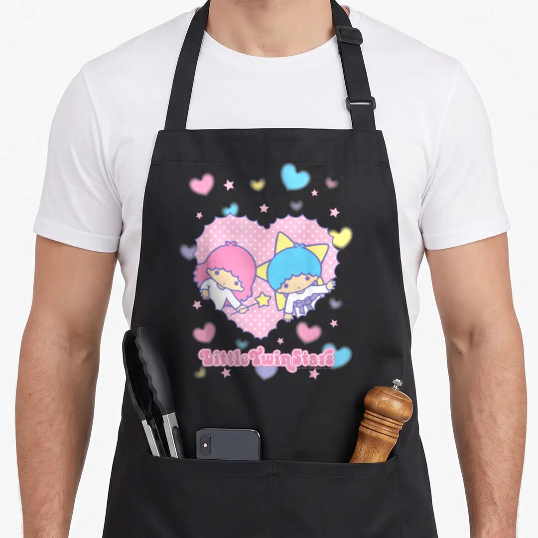 Twin valentine apron - Two cartoon characters inside pink polka-dot heart with scattered stars and text below — shown on a black cotton canvas apron against a white background
