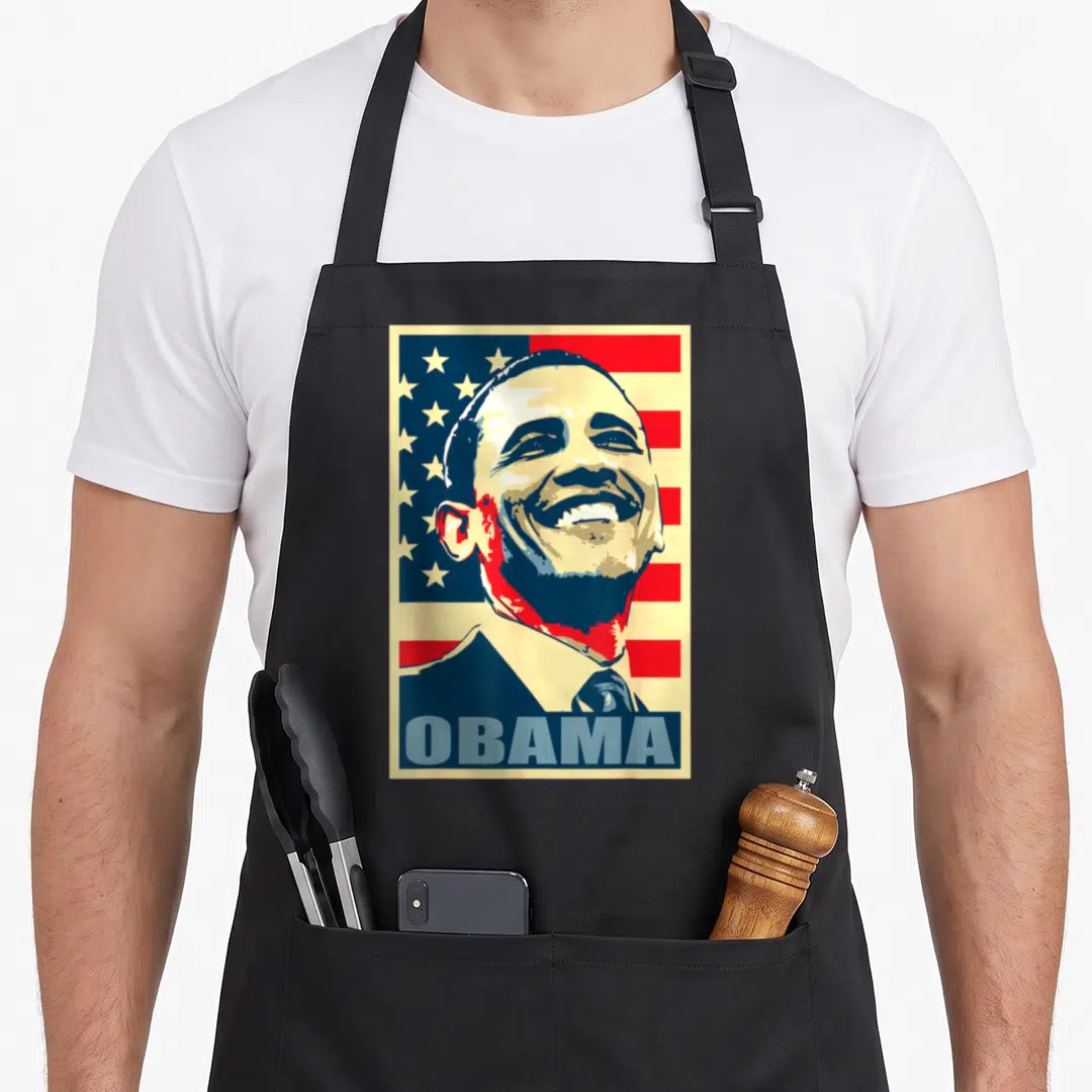Barack american flag apron - Stylized smiling portrait of Obama on flag background with blue OBAMA text bar — shown on a black cotton canvas apron against a white background