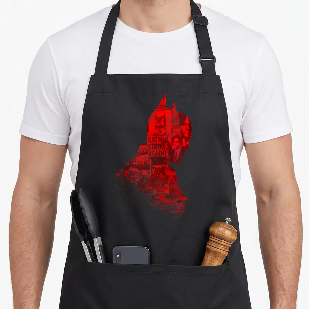 Silhouette novelty apron - Red silhouette of Batman head filled with newspaper collage and text BATMAN STRIKES AGAIN!! — shown on a black cotton canvas apron against a white background
