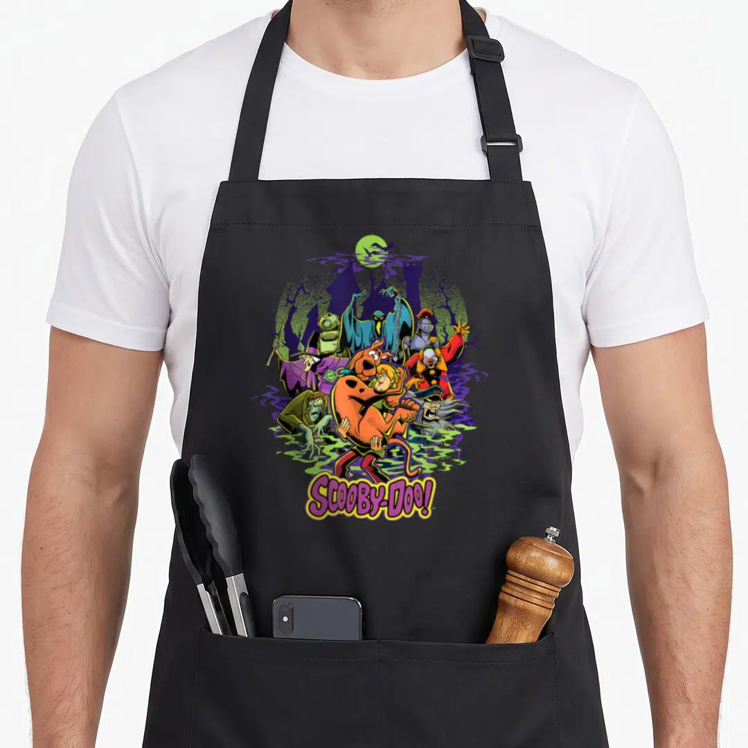 Shaggy decade apron - Cartoon Scooby-Doo and Shaggy running from monsters like a clown and knight near a purple castle — shown on a black cotton canvas apron against a white background