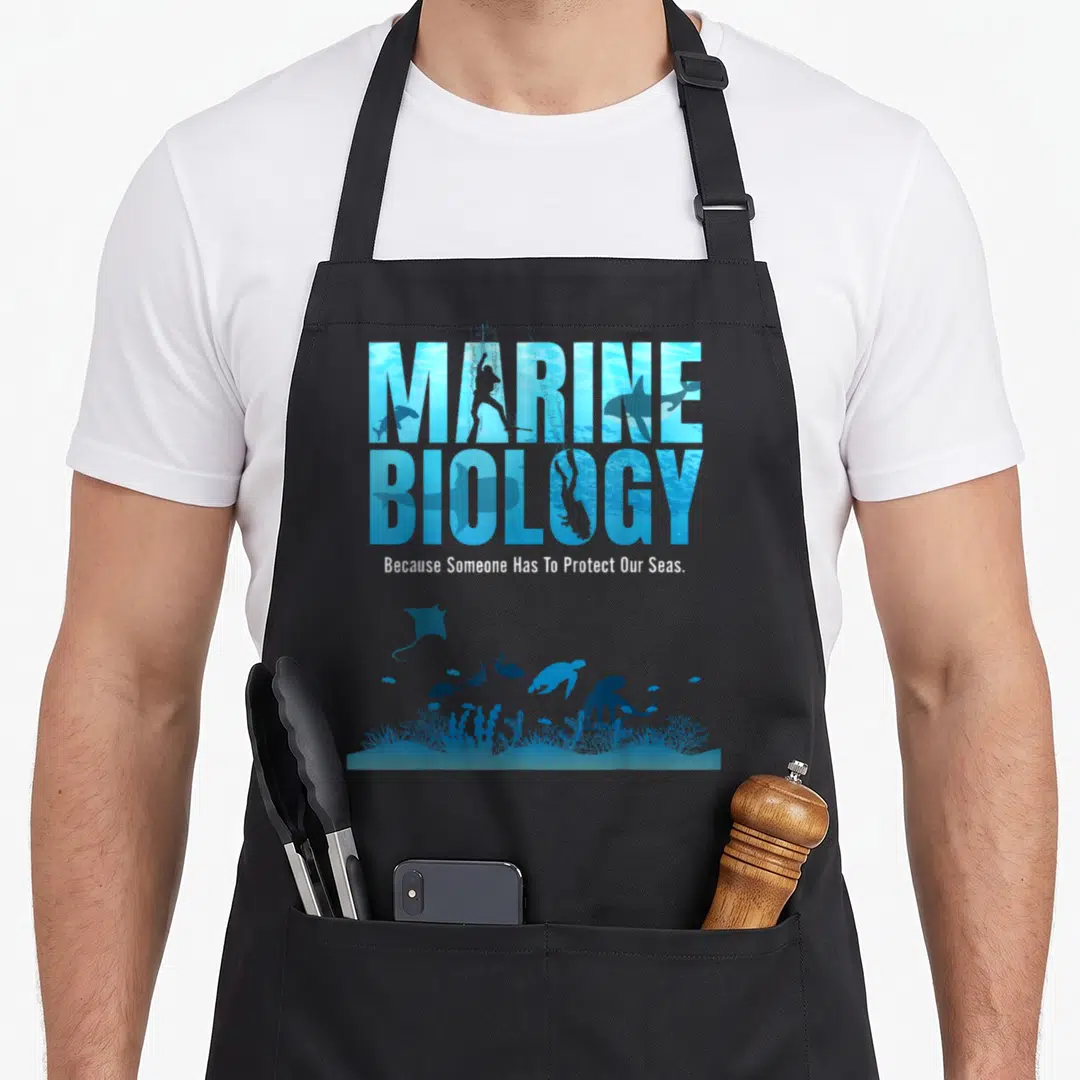 Marine biologist apron - Stacked text filled with divers and sharks above coral reef silhouettes in blue and white — shown on a black cotton canvas apron against a white background