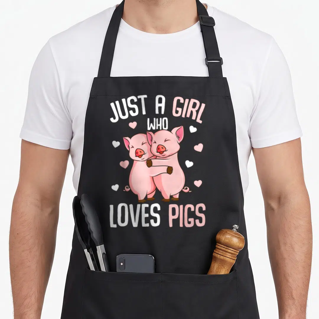 Vintage pig lover apron - Two pink cartoon pigs hugging with scattered hearts and text JUST A GIRL WHO LOVES PIGS — shown on a black cotton canvas apron against a white background
