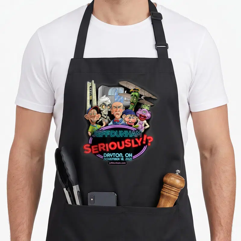 Jeff dayton apron - Puppet cluster above stacked neon text reading Jeff Dunham seriously Dayton Ohio — shown on a black cotton canvas apron against a white background
