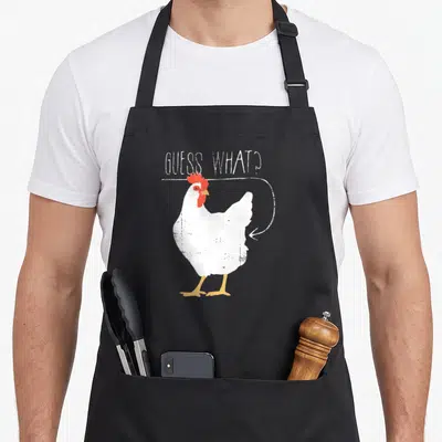 Guess butt chicken apron - White cartoon chicken with red comb orange legs white arrow pointing to rear under GUESS — shown on a black cotton canvas apron against a white background