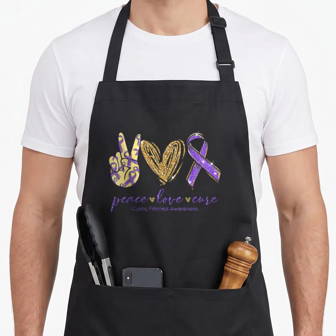 Cystic ribbon apron - Purple and gold peace hand heart ribbon with peace love cure text — shown on a black cotton canvas apron against a white background