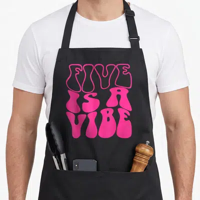 Five 5th birthday apron - Pink wavy typography reading FIVE IS A VIBE stacked vertically — shown on a black cotton canvas apron against a white background
