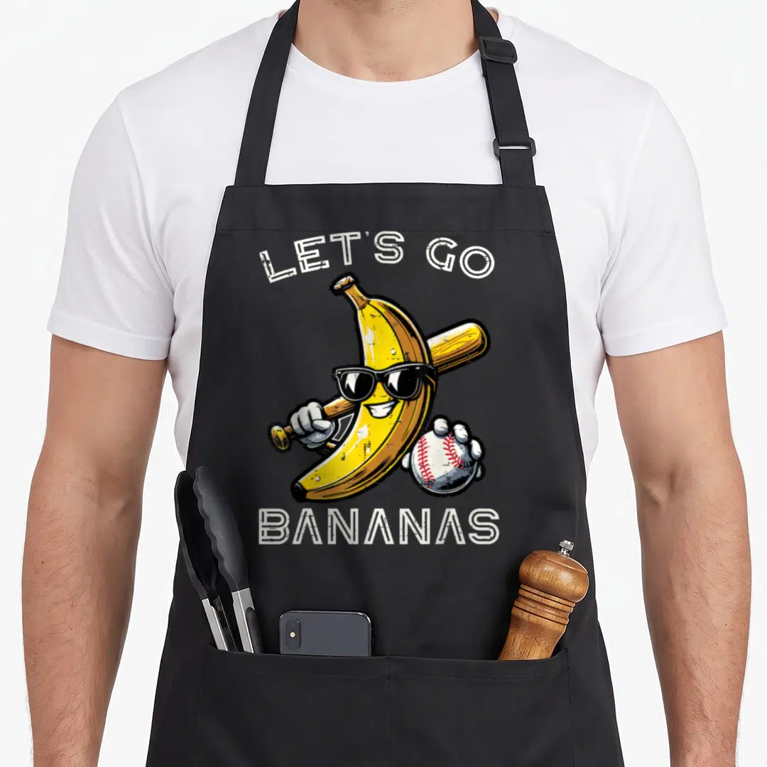 Youth banana apron - Cartoon banana with sunglasses holding a bat and baseball under white text — shown on a black cotton canvas apron against a white background
