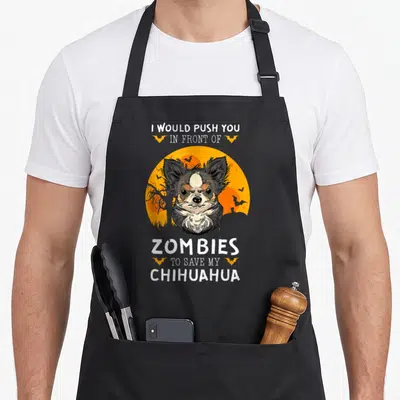 Halloween top dog aprons - Chihuahua face on orange moon with bats and white text about saving dog from zombies — shown on a black cotton canvas apron against a white background