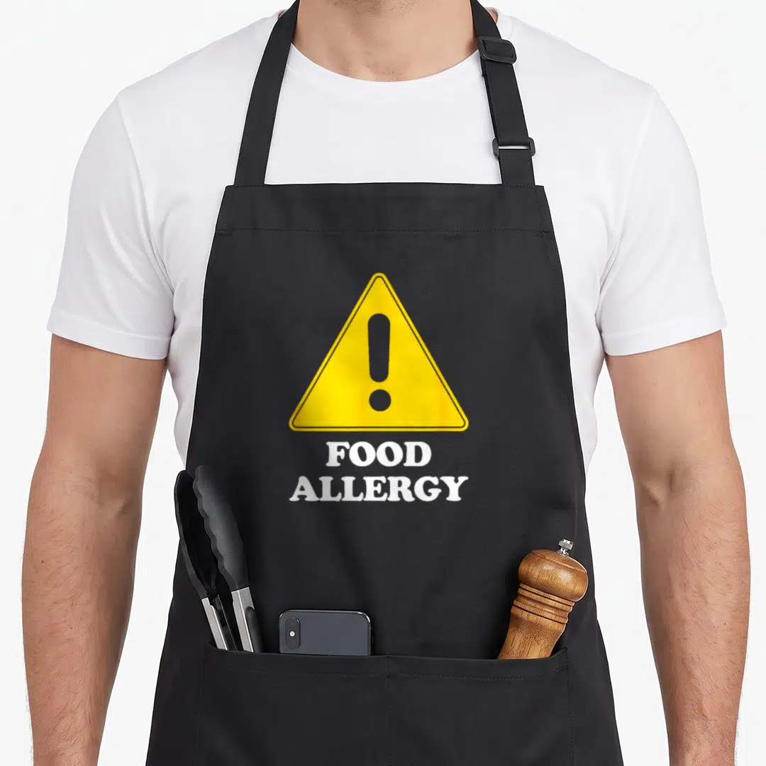 Allergy food aprons - Yellow warning triangle with exclamation mark and stacked FOOD ALLERGY text on grey background — shown on a black cotton canvas apron against a white background