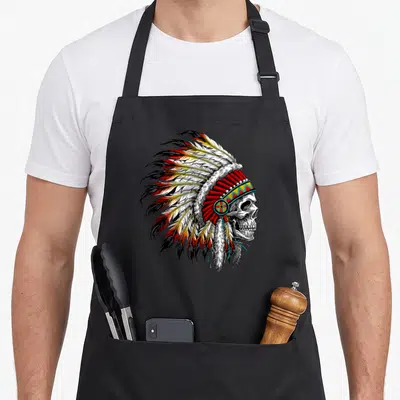 Chief native american apron - Realistic skull wearing red white yellow and black feathered war bonnet with beaded — shown on a black cotton canvas apron against a white background