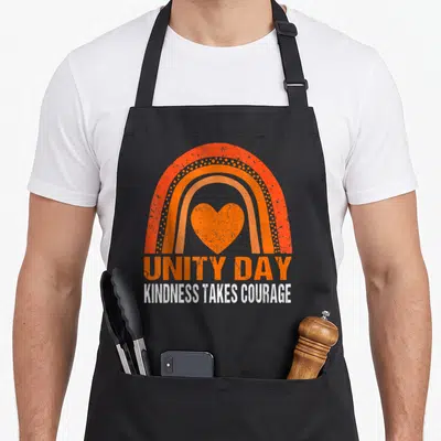 Courage novelty apron - Orange rainbow arch with heart and UNITY DAY text — shown on a black cotton canvas apron against a white background