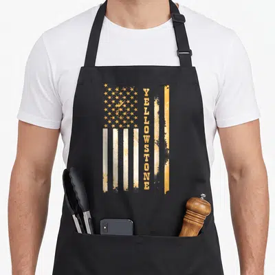 Flag stone apron - Vertical YELLOWSTONE text overlaid on distressed yellow-orange and white USA flag — shown on a black cotton canvas apron against a white background