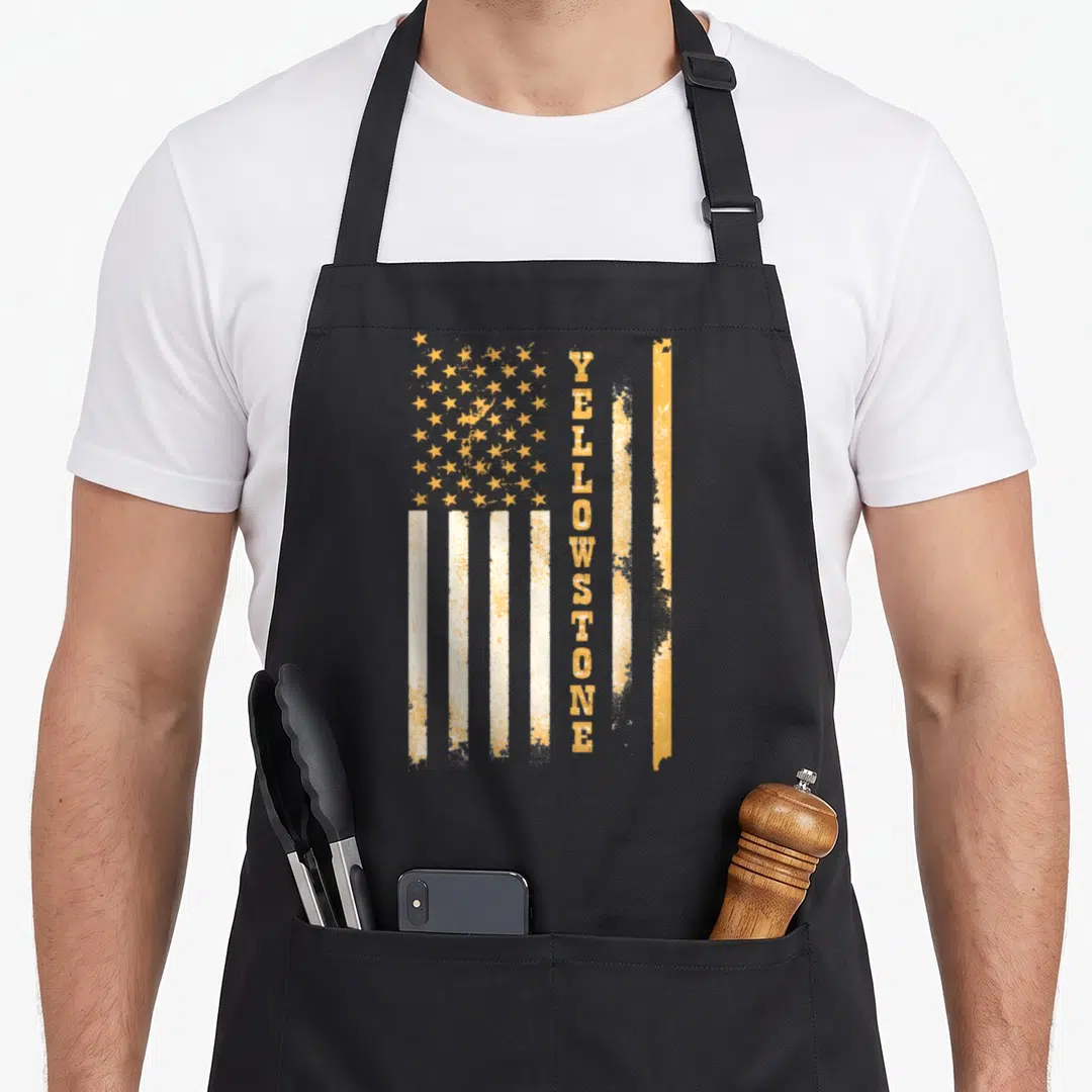 Flag stone apron - Vertical YELLOWSTONE text overlaid on distressed yellow-orange and white USA flag — shown on a black cotton canvas apron against a white background