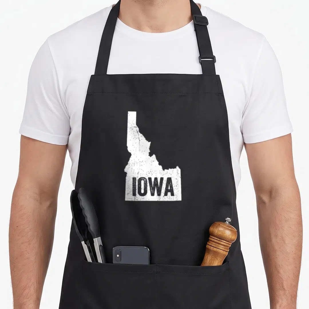 Idaho joke apron - Distressed white Idaho map silhouette with grey Iowa text label — shown on a black cotton canvas apron against a white background