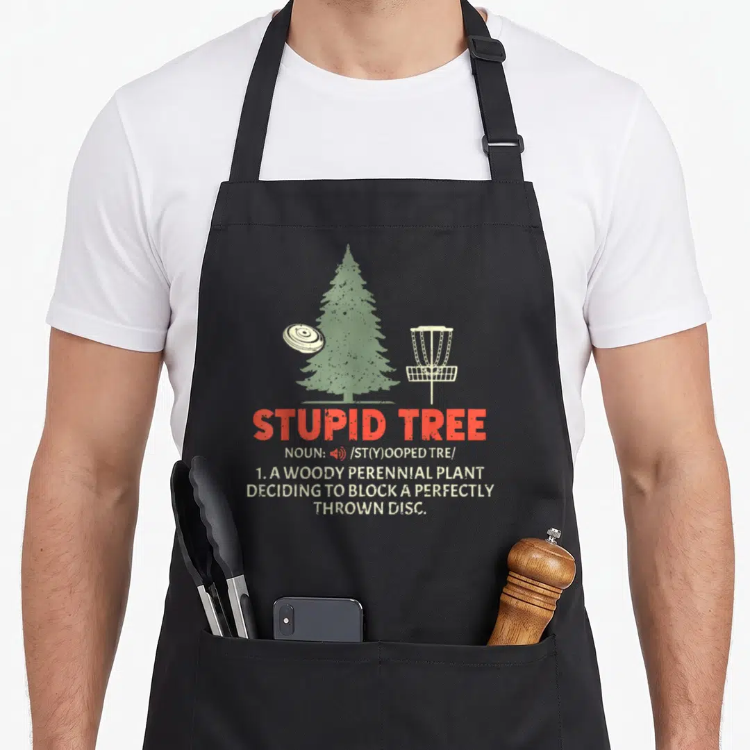 King golf apron - Red Stupid Tree definition text below green tree and white disc golf basket illustration — shown on a black cotton canvas apron against a white background