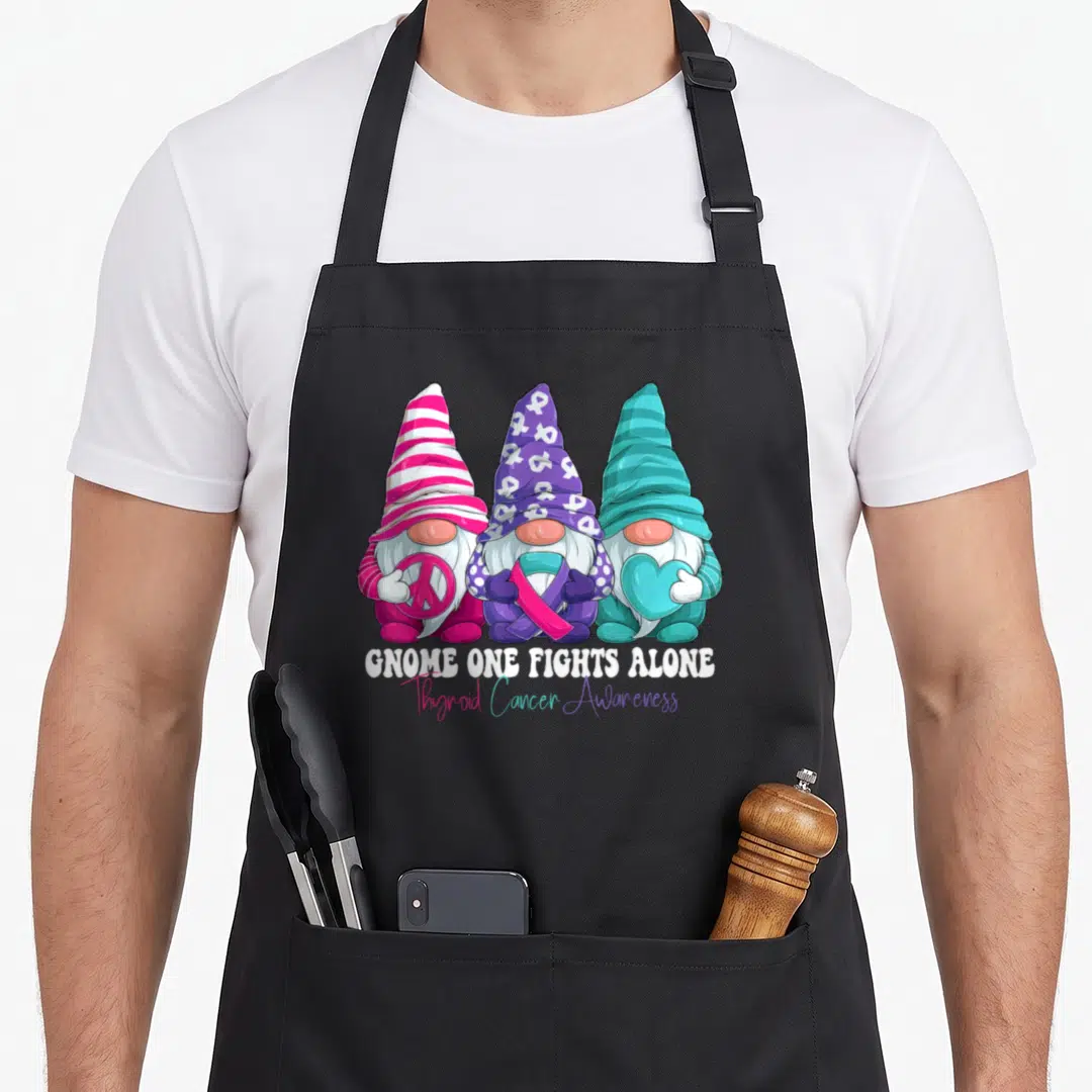 Gnomy thyroid apron - Three gnomes holding peace sign, ribbon, and heart with Gnome One Fights Alone text — shown on a black cotton canvas apron against a white background