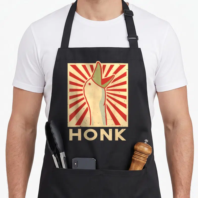 Honk goose apron - Retro goose head in red and beige sunburst square with HONK text below — shown on a black cotton canvas apron against a white background