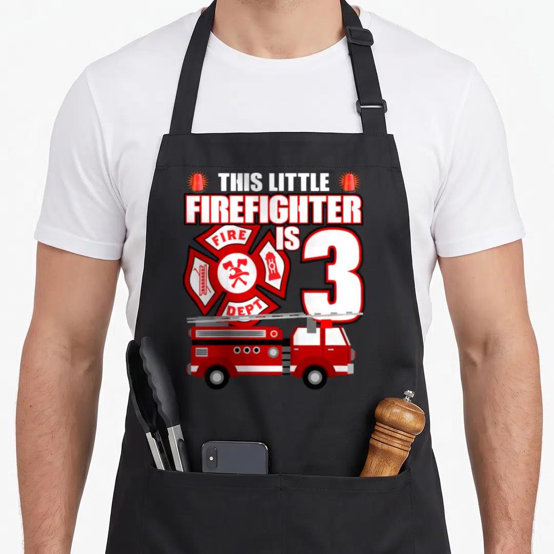 Firefighter birthday truck apron - This Little Firefighter Is 3 text above red fire truck and department emblem — shown on a black cotton canvas apron against a white background