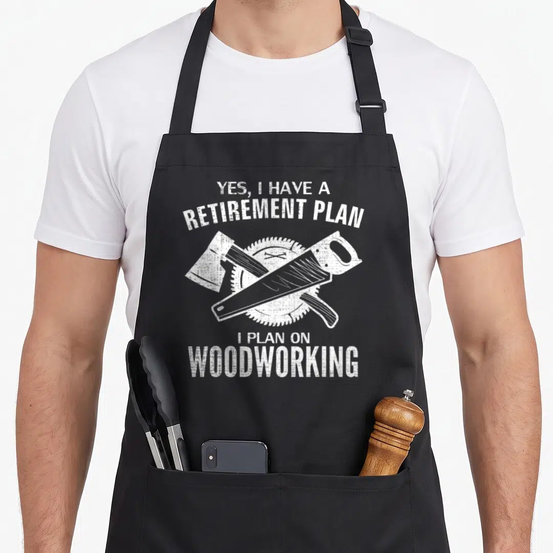 Retirement woodworking apron - White distressed text yes i have a retirement plan above crossed axe and hand saw — shown on a black cotton canvas apron against a white background